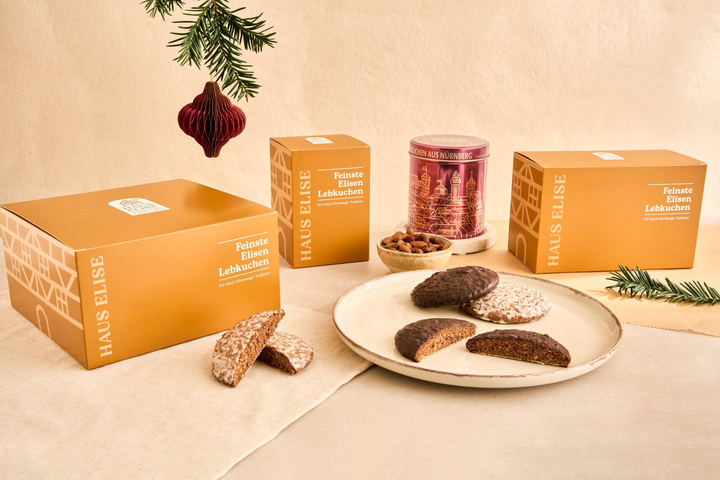 HAUS ELISE Geschenkboxen mit 6, 12 und 20 Elisen-Lebkuchen, die Dose Kaiserburg in Bordeaux, eine Schale Haselnüsse und ein Teller mit schokolierten und glasierten Lebkuchen, dazu Tannenzweig und Christbaumkugel