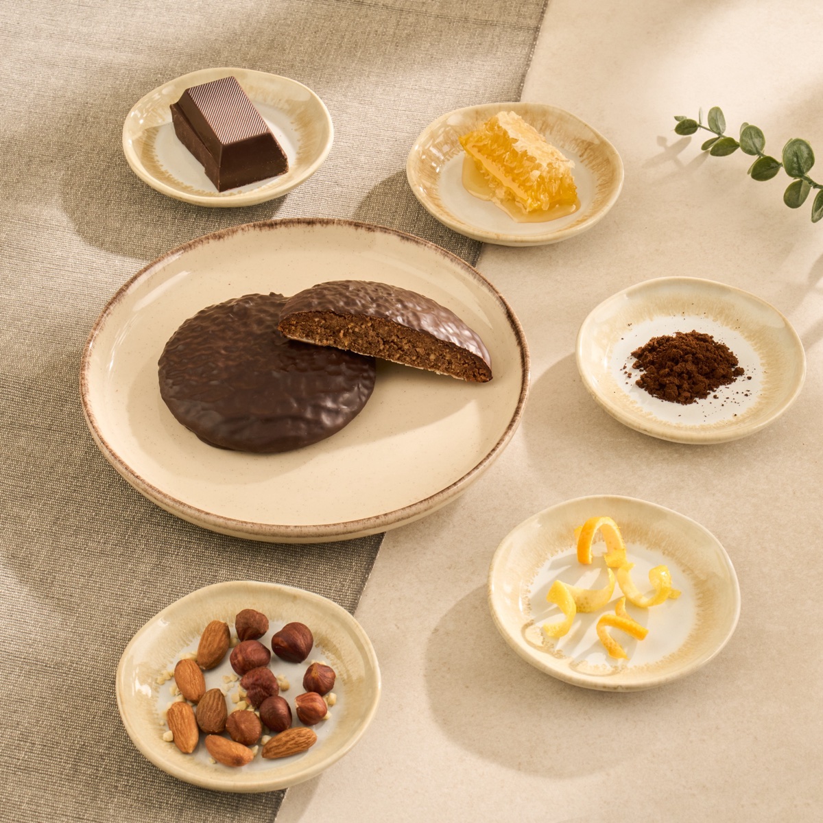 Angeschnittener schokolierter HAUS ELISE Elisen-Lebkuchen, umgeben von Zartbitterschokolade, Honig, Gewürzen, Orangen- und Zitronenschale, Haselnüssen und Mandeln